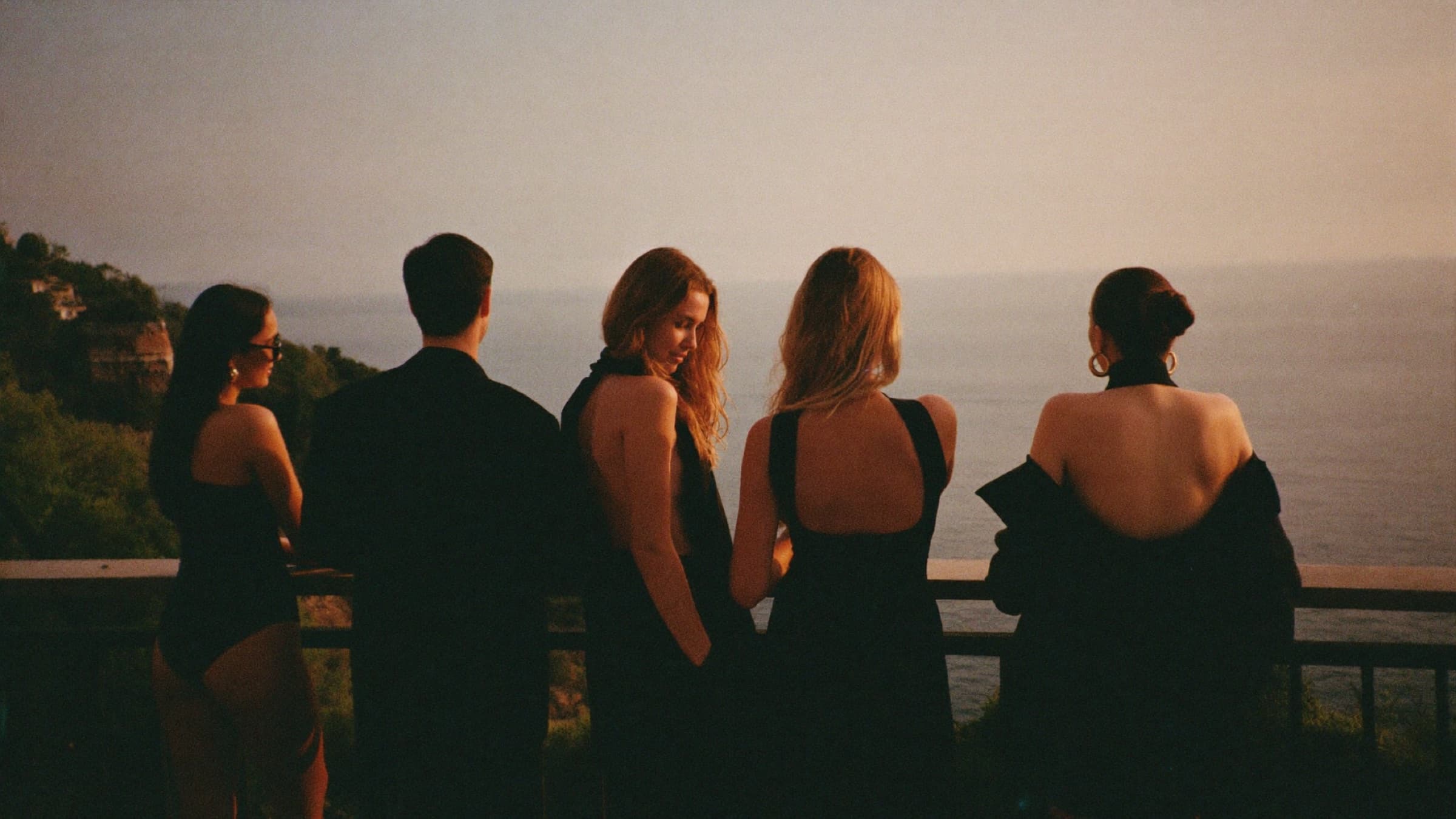 Friends at a Mediterranean clifftop terrace looking out to sea at dusk
