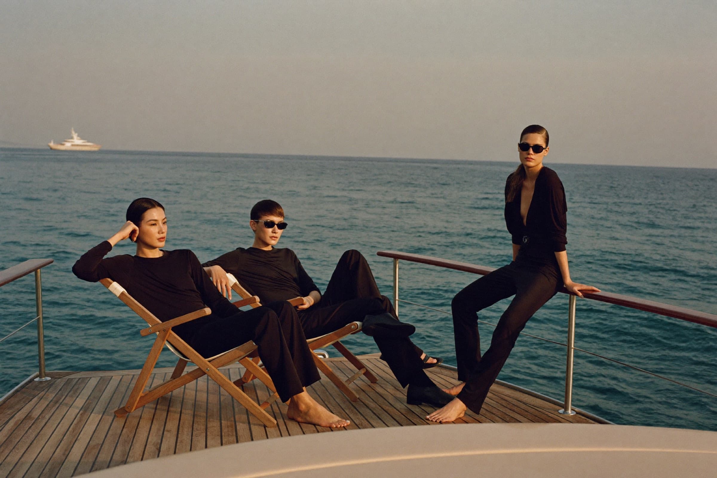 Friends in head-to-toe black on a Riviera yacht deck off Saint-Tropez at golden hour
